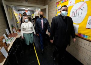 Mayor Adams walking School hallway with Fr Carlos and staff